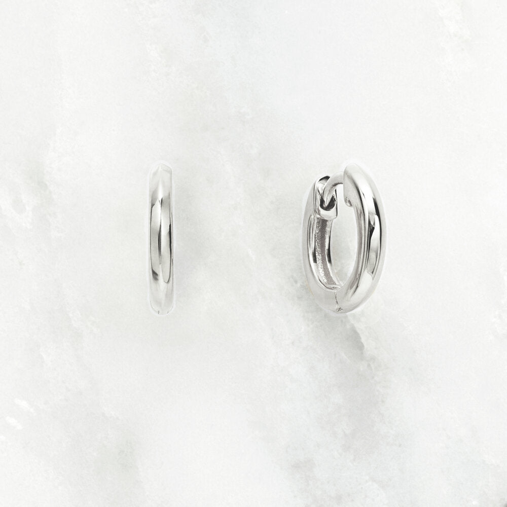 Silver small rounded plain huggie hoop earrings on a marble surface