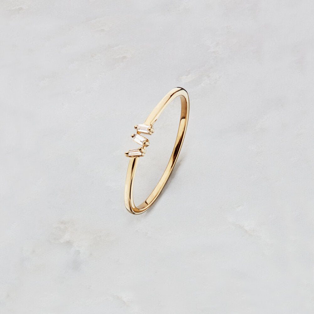 Gold diamond style three baguette ring on hand on a marble surface