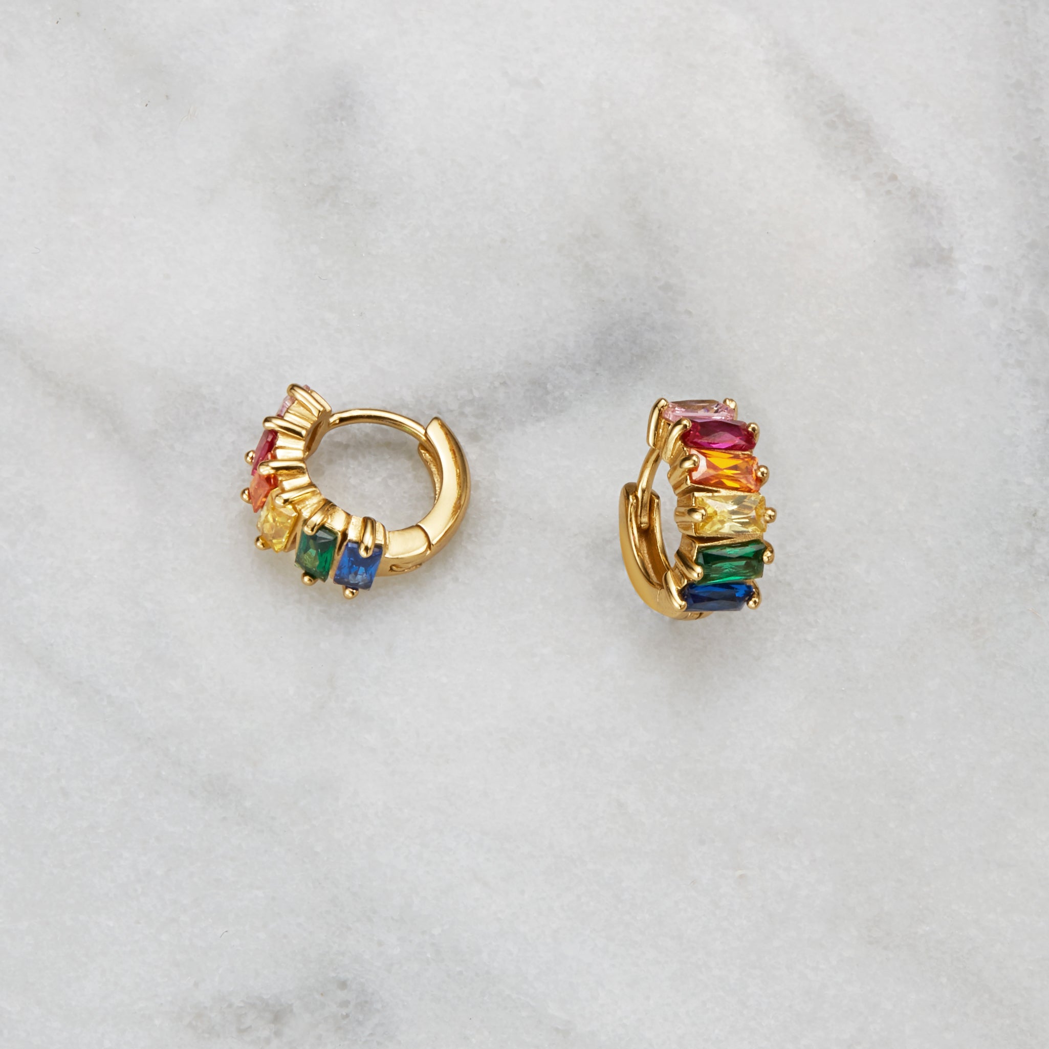 Gold rainbow gemstone cluster huggie hoop earrings on a marble surface