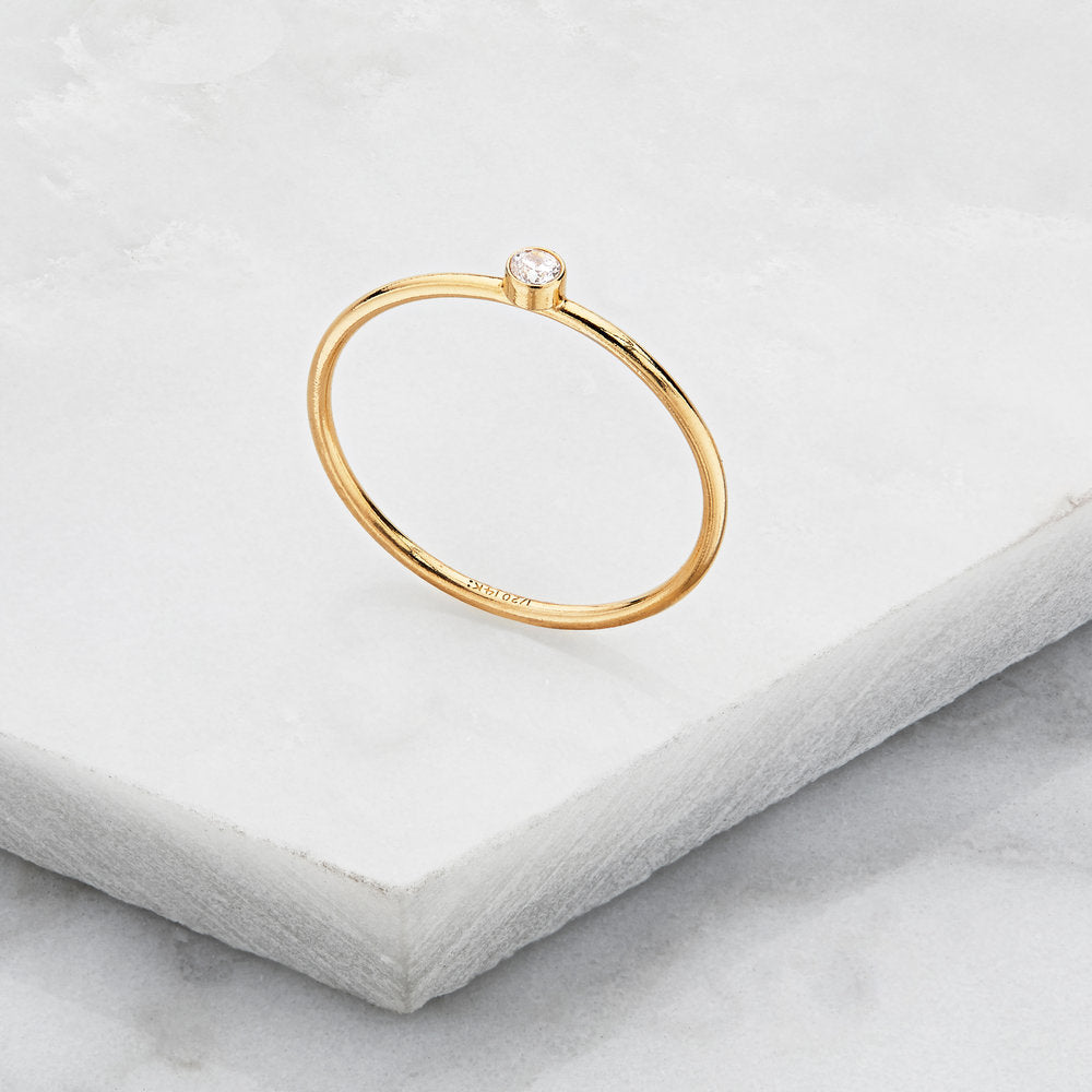 Gold thin diamond style stacking ring upright on a marble surface