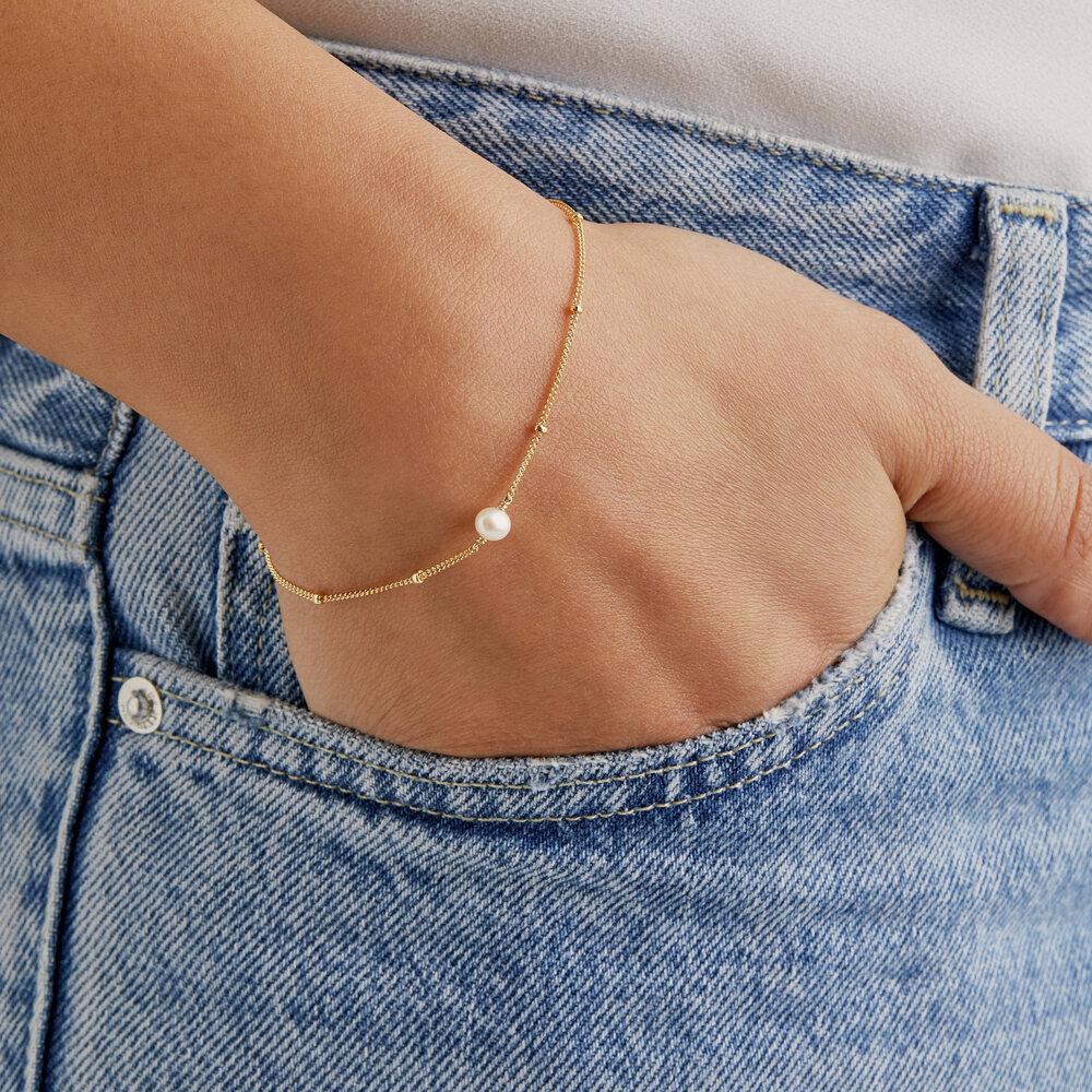 Gold satellite pearl bracelet on a wrist with fingers in a denim blue pocket