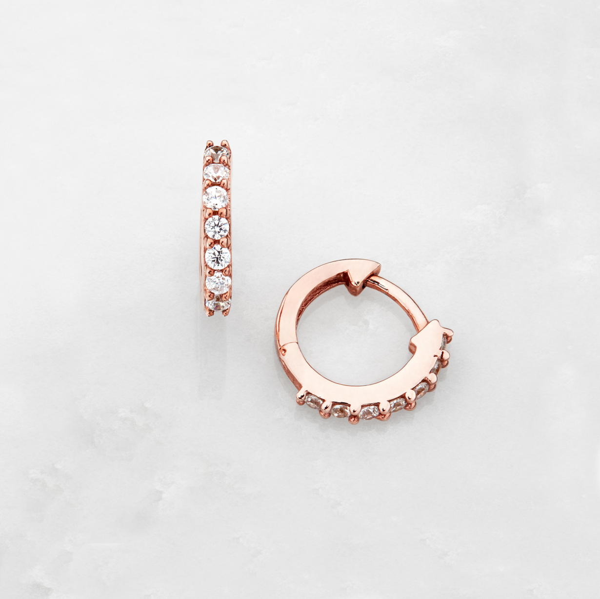 Rose gold huggie pearl drop earrings on a marble surface
