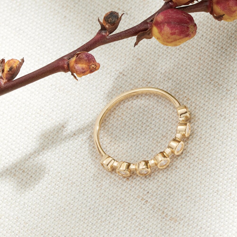 Gold diamond style round eternity ring on a woven surface with a plant