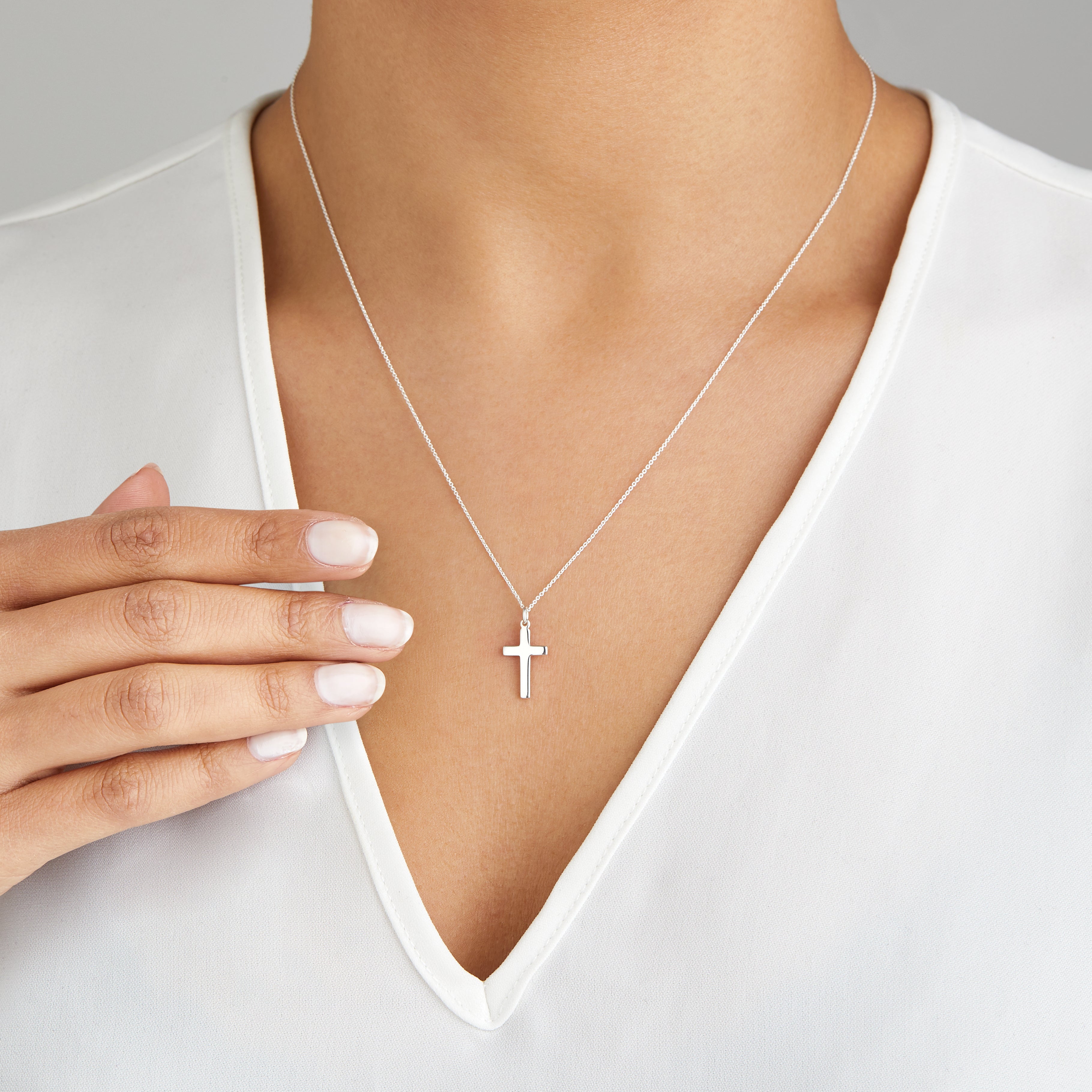 Silver cross necklace around a neck with a white V-neck top