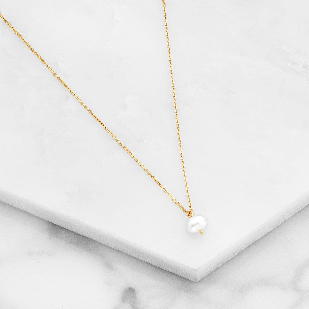 Gold pearl drop necklace on marble surfaces