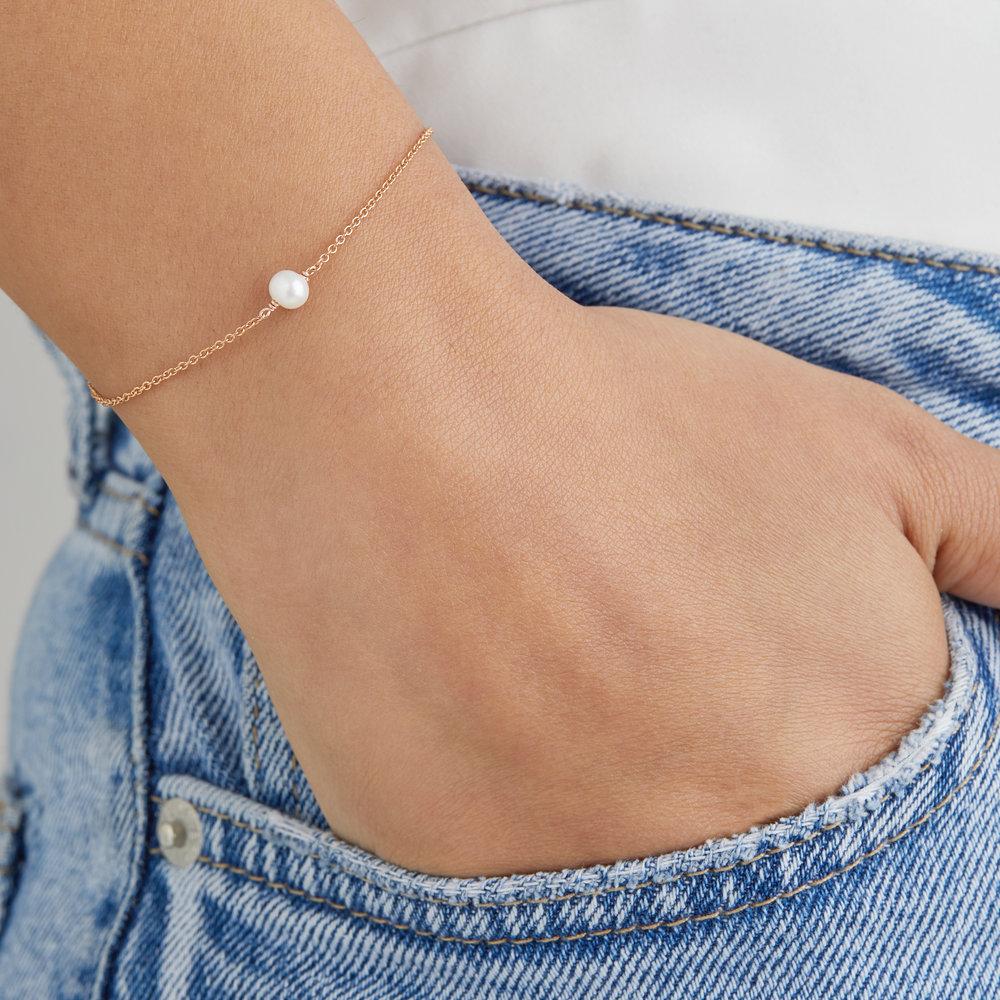 Gold single pearl bracelet around a wrist with the fingers in a denim blue pocket
