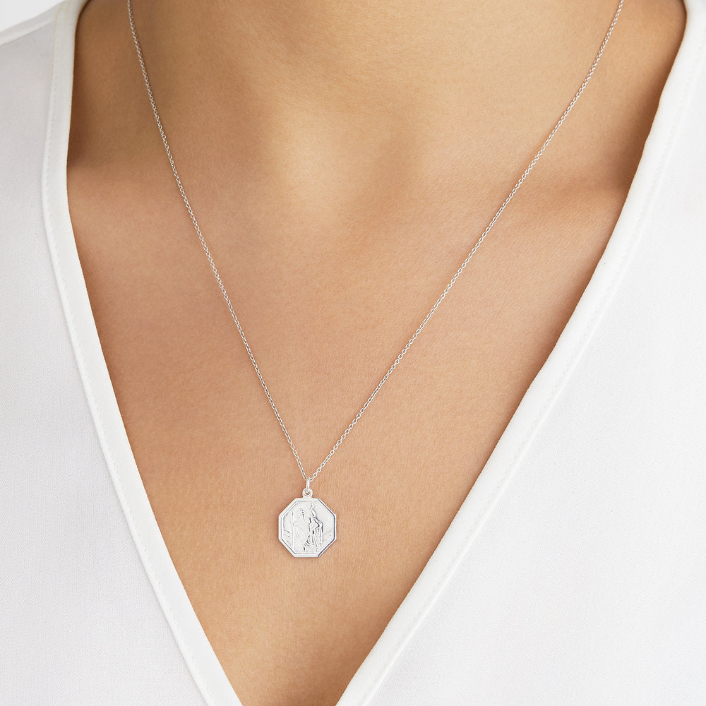 Silver St Christopher octagonal medallion necklace around a neck of a woman wearing a white V neck top