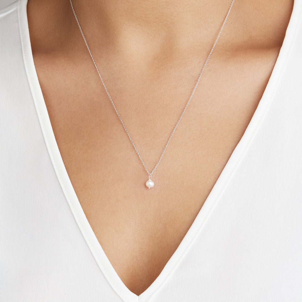 Silver single pearl necklace worn around the neck of a woman in a white V-neck top