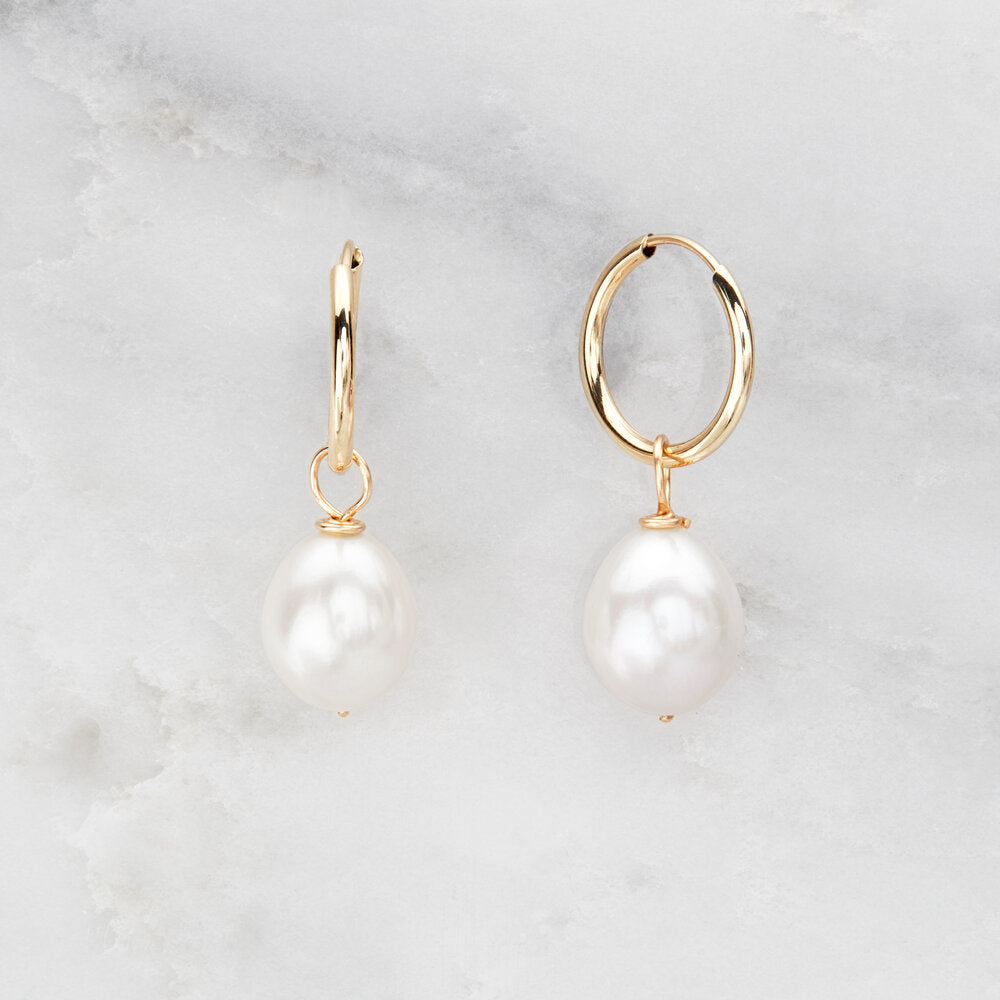 Solid gold large pearl drop hoop earrings on a marble background