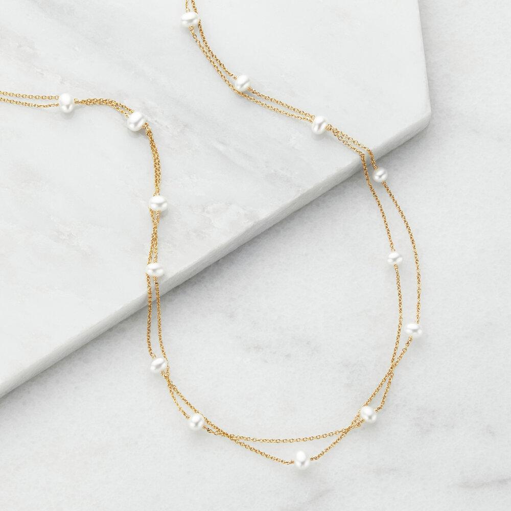 Gold layered pearl necklace on marble surfaces