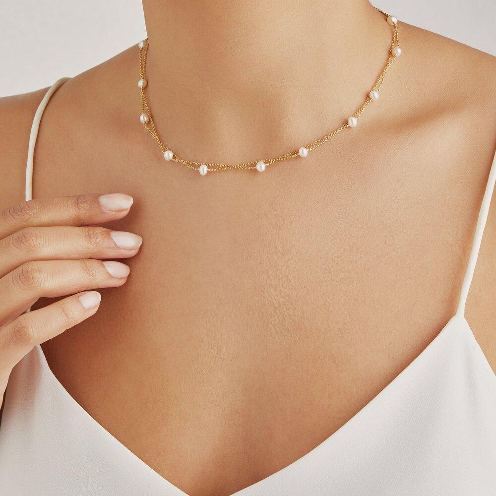 Gold layered pearl necklace around a neck with a white top