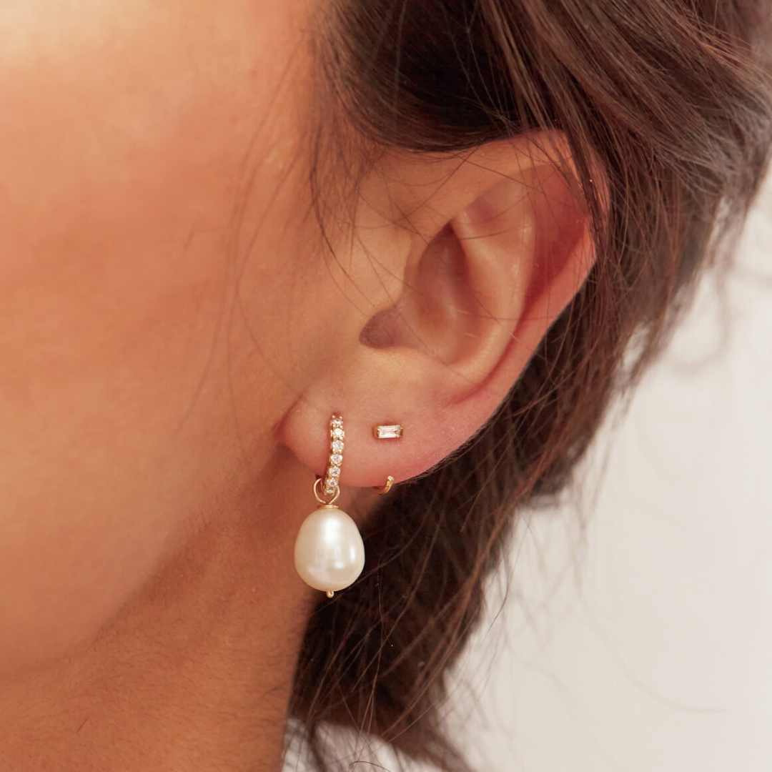 Gold diamond style baguette lobe hoop earring and a gold huggie pearl drop earring in one ear lobe close up