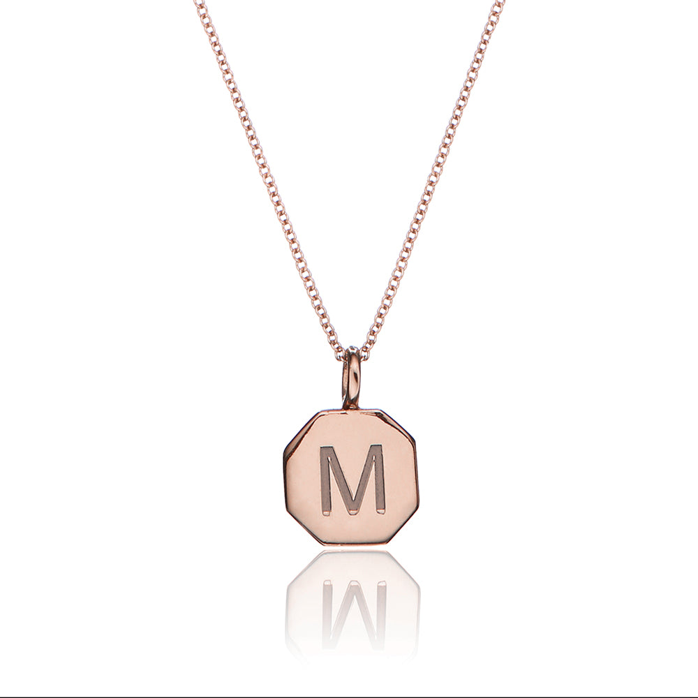 Rose gold personalised hexagon necklace with the letter 'M' engraved on it on a white background