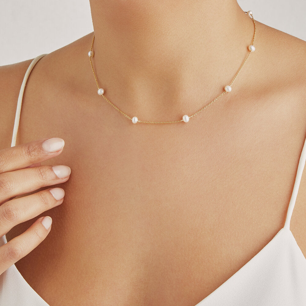 Gold ten pearl choker around a neck of a woman wearing a white strappy top