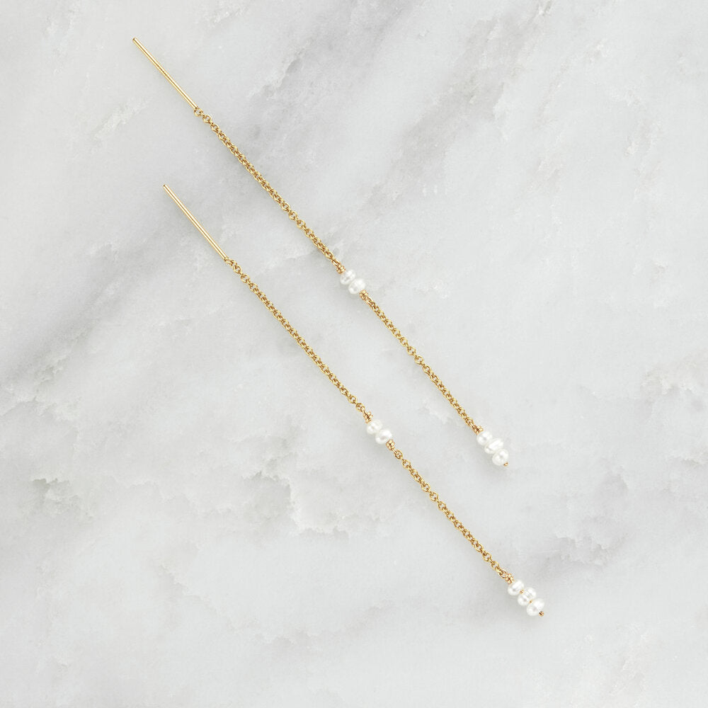 Gold mini pearl ear threaders on a marble surface