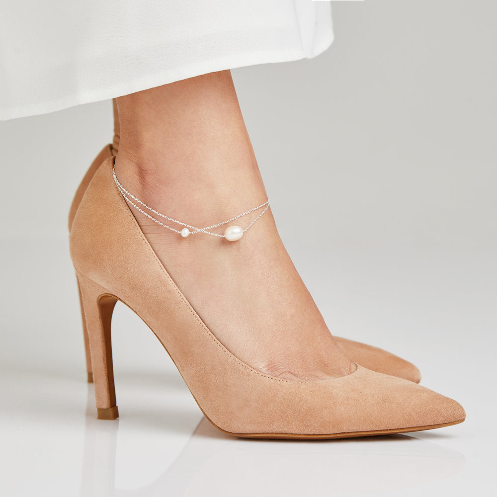 Gold layered large and small pearl anklet on ankle wearing beige heels and white trousers