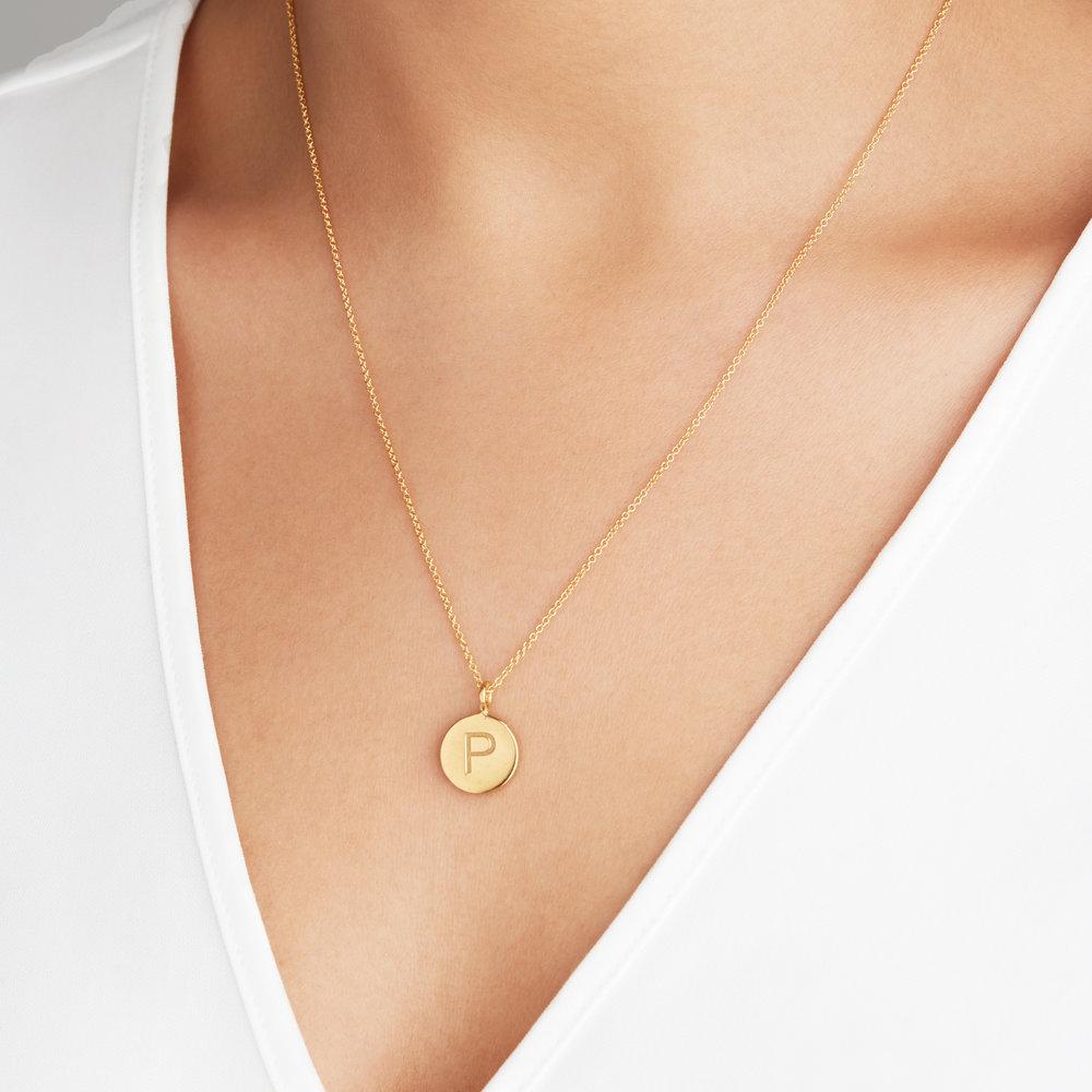 Gold large engraved disc necklace with P engraved around a neck wearing a white v neck top