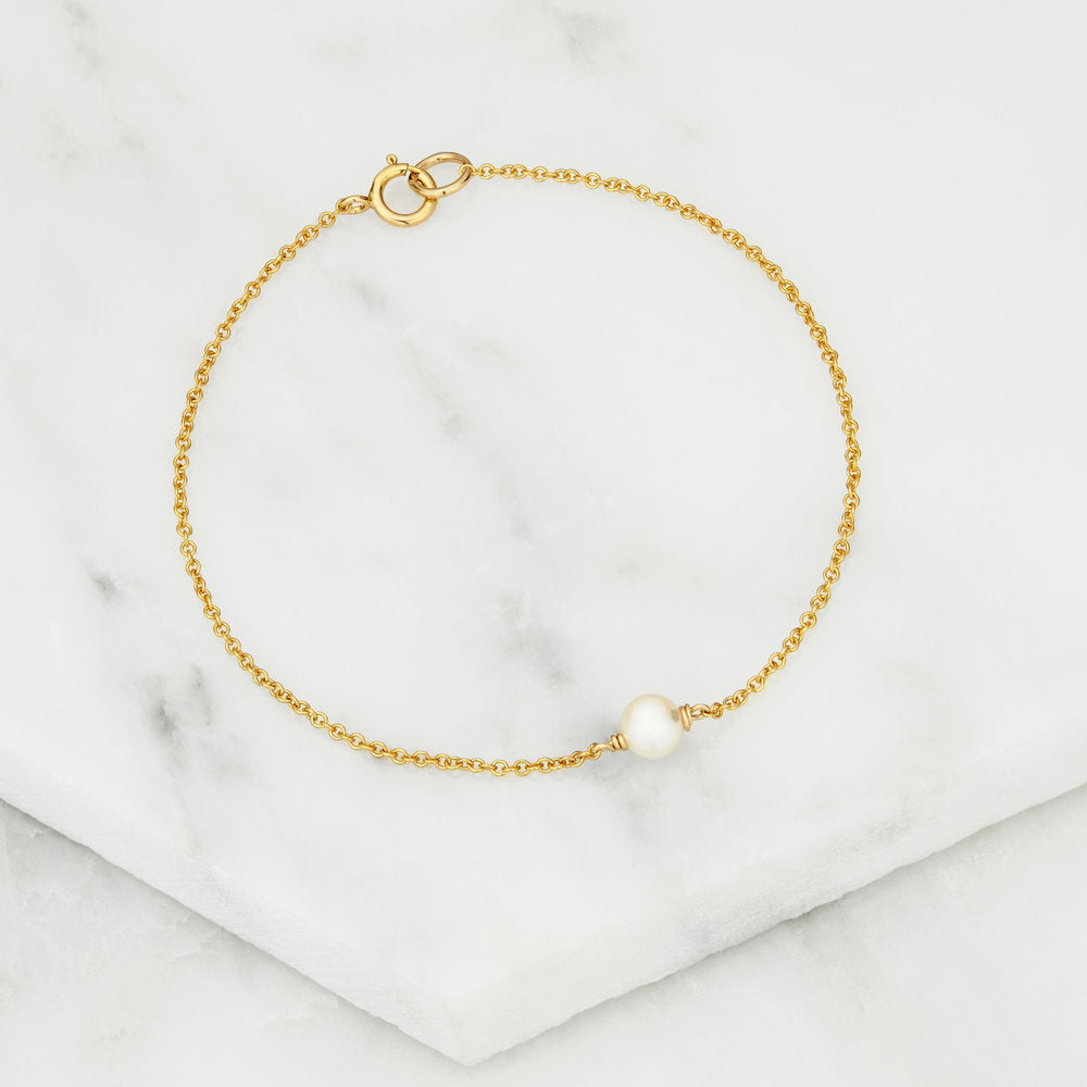 Gold single pearl bracelet on a marble surface