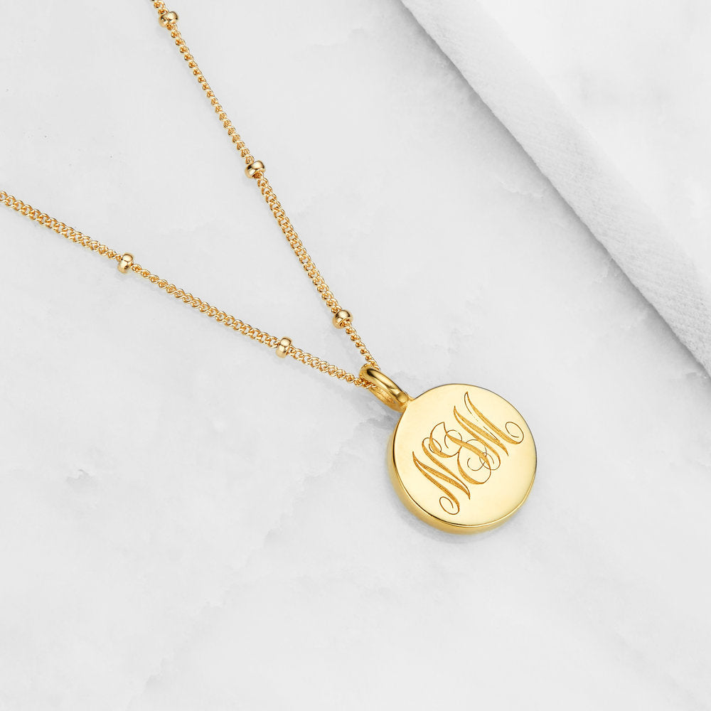 Gold large engraved disc necklace with N&M engraved on marble surface