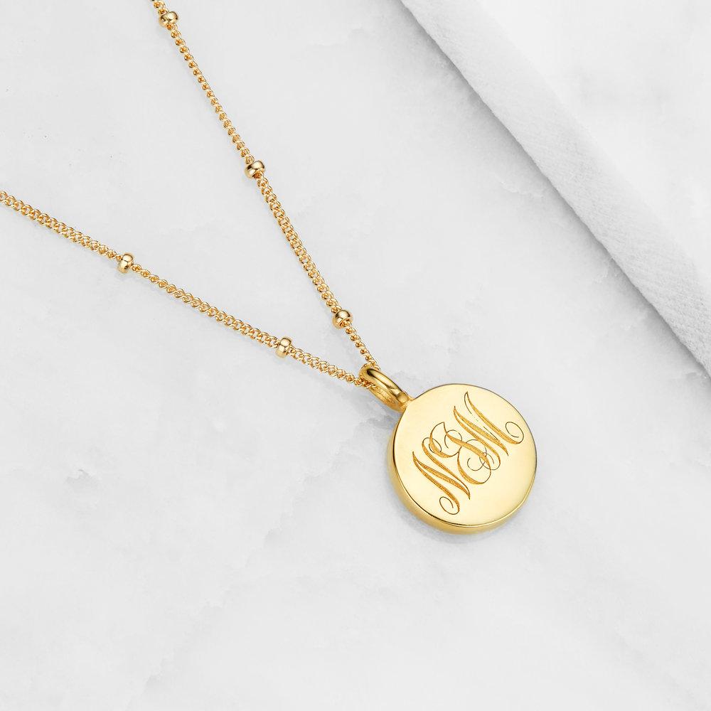 Gold large engraved disc necklace with N&M engraved on marble surface