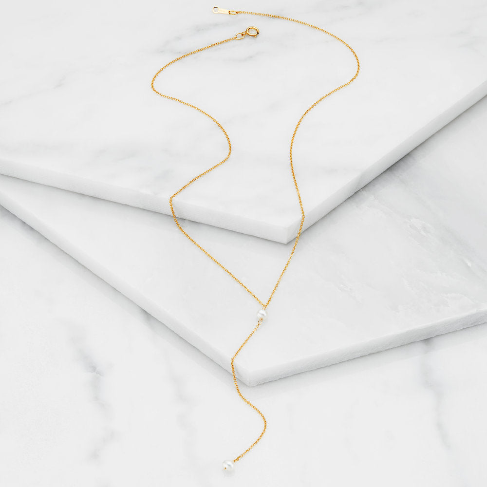 Gold pearl lariat necklace on marble surfaces